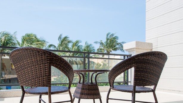 A balcony with wicker chairs and a table, overlooking palm trees and a building. - Have FUN villa (Hengchun)