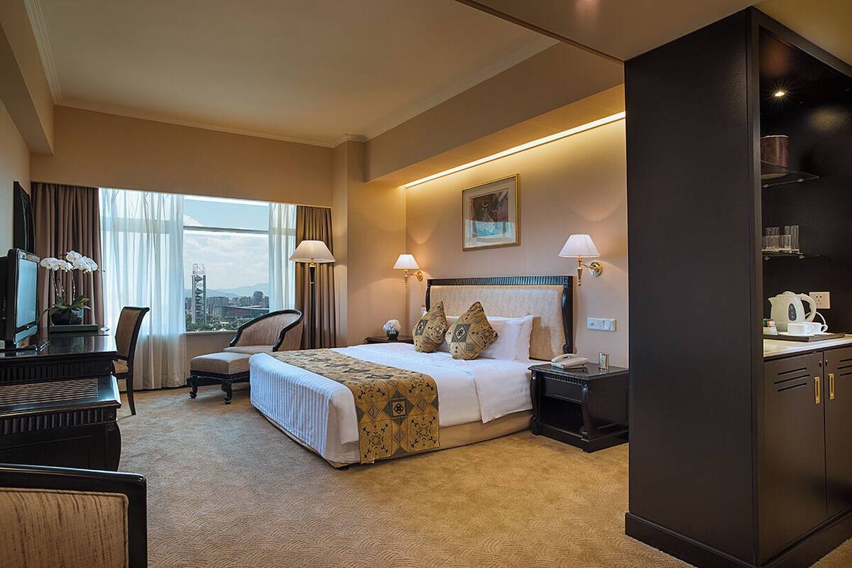 Habitación de hotel con una cama grande, dos mesitas de noche, un escritorio con una silla, un piano y vista a la ciudad.