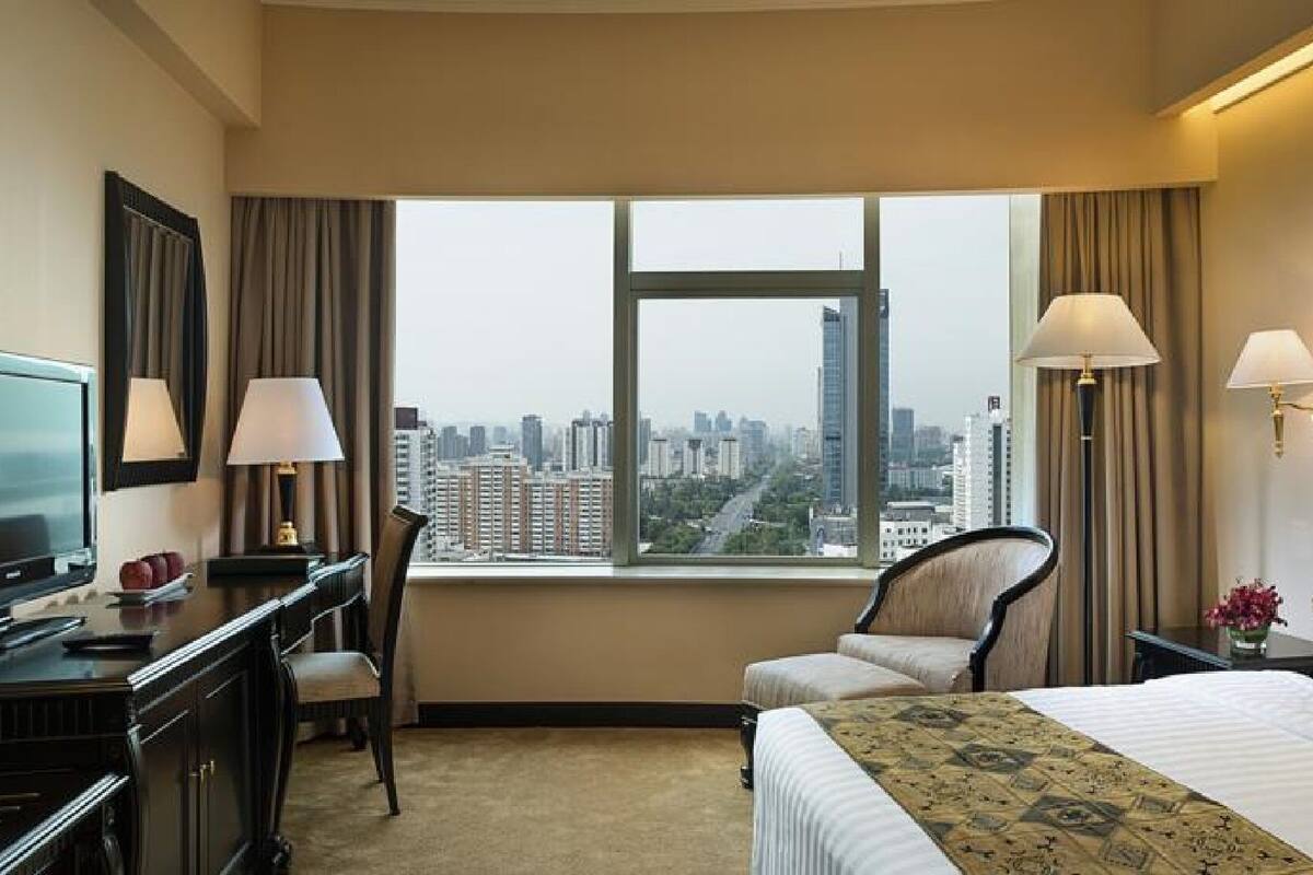 Habitación de hotel con cama, escritorio, silla, televisión y vistas a la ciudad.