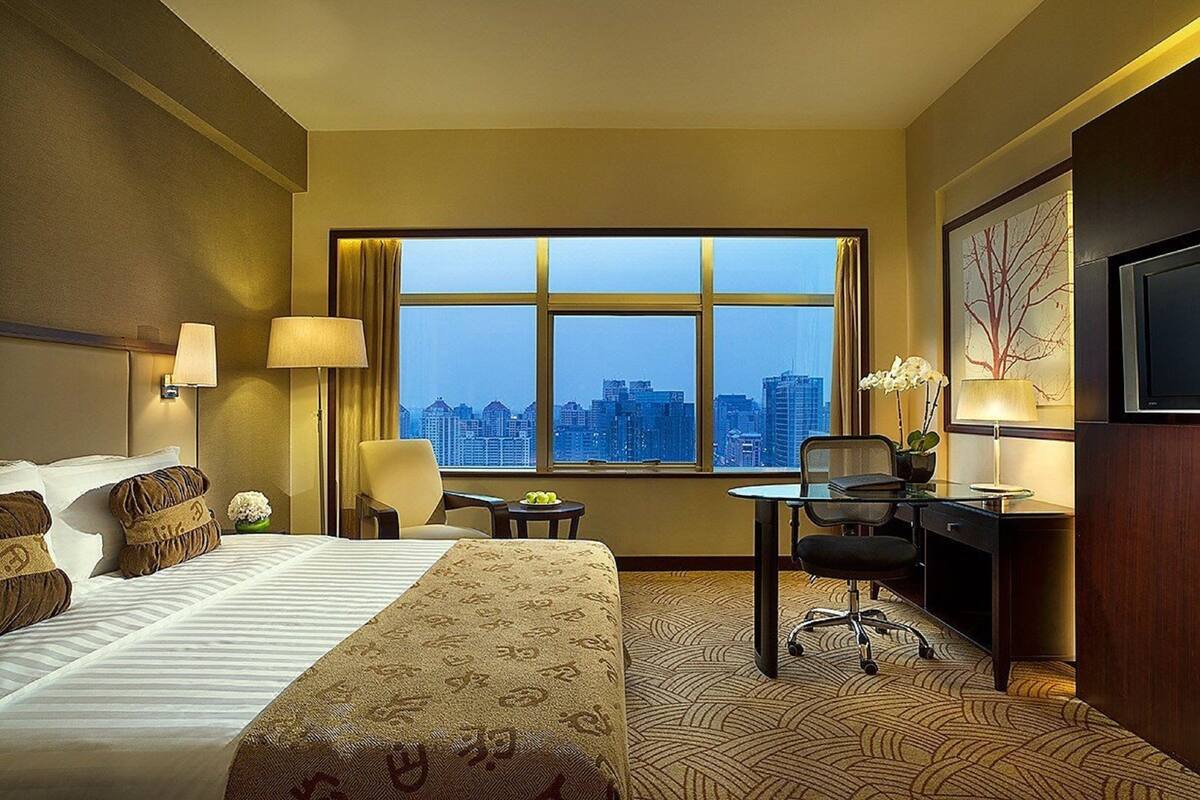 Una habitación de hotel con un ventanal grande, una cama, un escritorio y una silla.