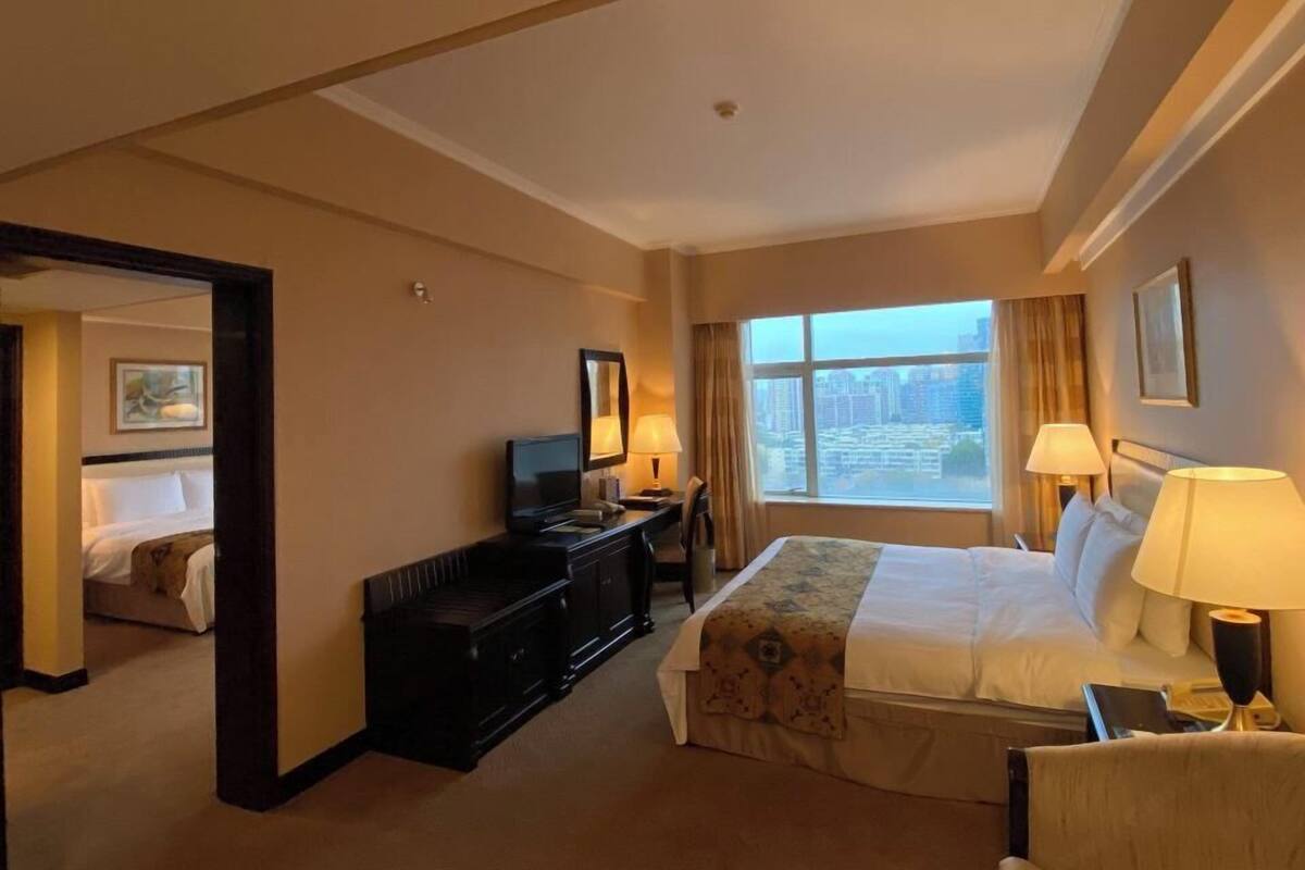 Habitación de hotel con cama, escritorio, silla, televisor y ventana con vista a la ciudad.