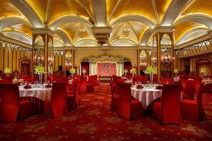A banquet hall with round tables and red chairs, ornate ceiling, and chandeliers. - Celebrity International Grand Hotel (Beijing)