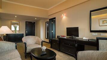 Habitación de hotel con zona de estar que incluye dos sillones, una mesa de centro, un televisor de pantalla plana, un aparador y un espejo.