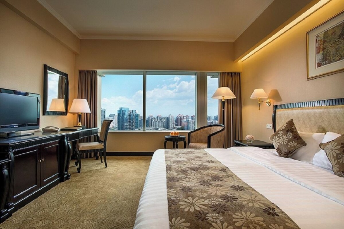 Ein Hotelzimmer mit Bett, Schreibtisch, Stuhl, Fernseher und Blick auf die Stadt.