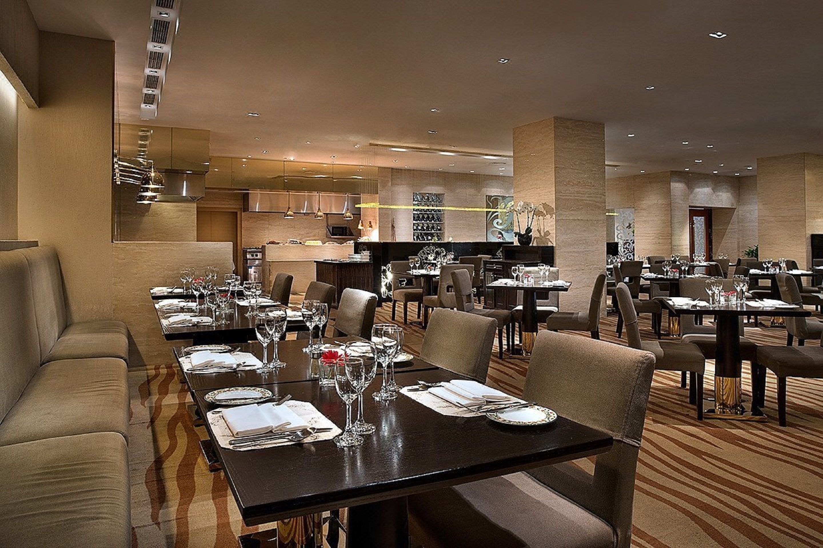 Un restaurante espacioso con varias mesas y sillas, un área de cocina al fondo y una decoración de estilo moderno.