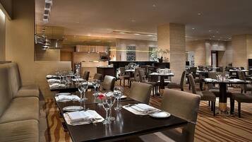 Un restaurante espacioso con varias mesas y sillas, un área de cocina al fondo y una decoración de estilo moderno.