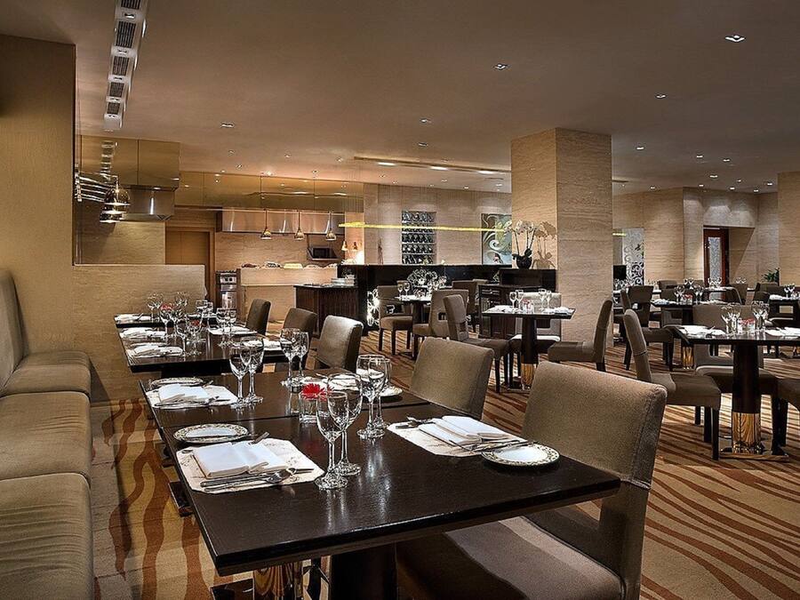Un restaurante espacioso con varias mesas y sillas, un área de cocina al fondo y una decoración de estilo moderno.