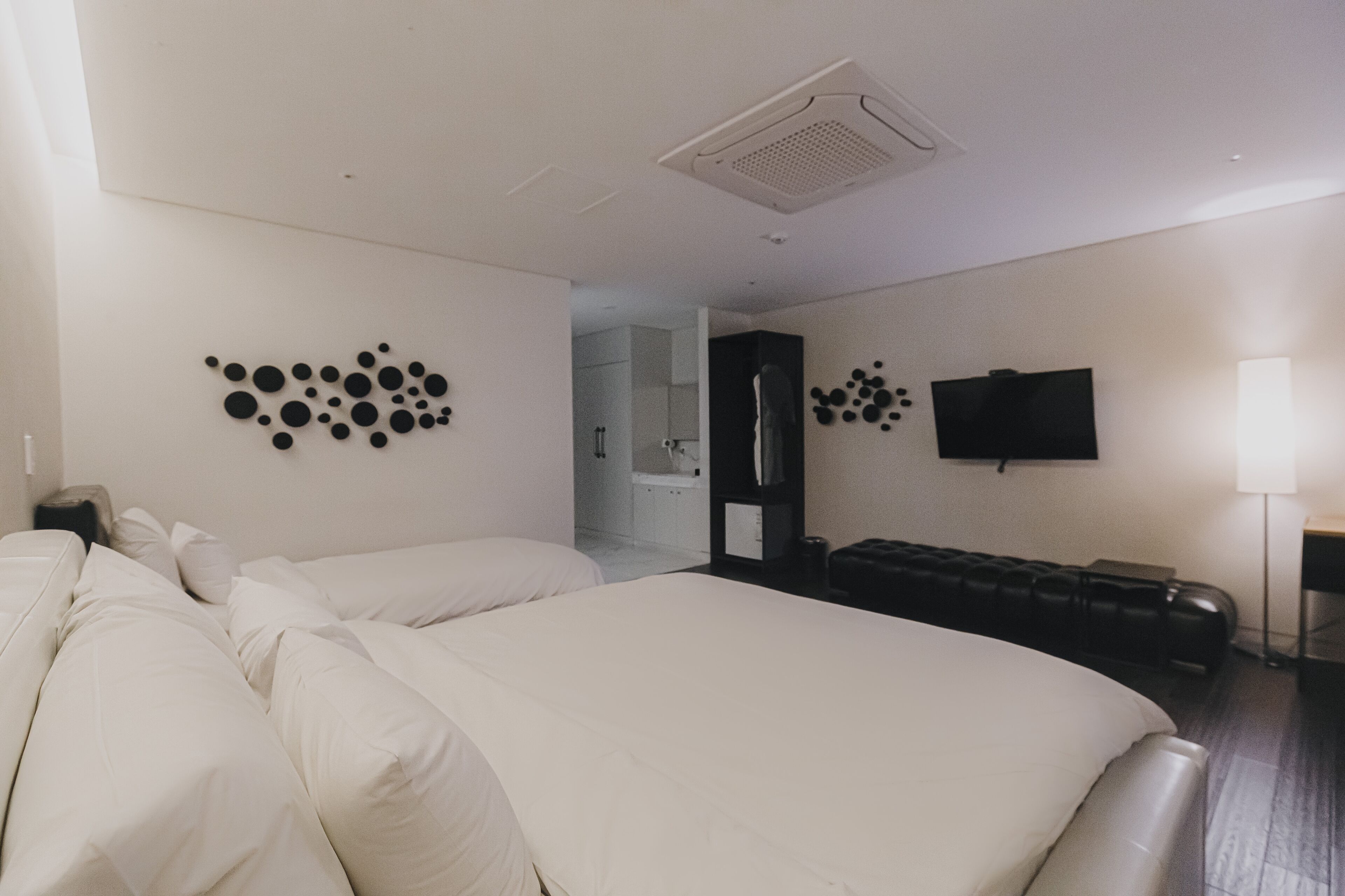 A modern hotel room with a large bed, a seating area, a flat-screen TV, and a bathroom visible through an open door.