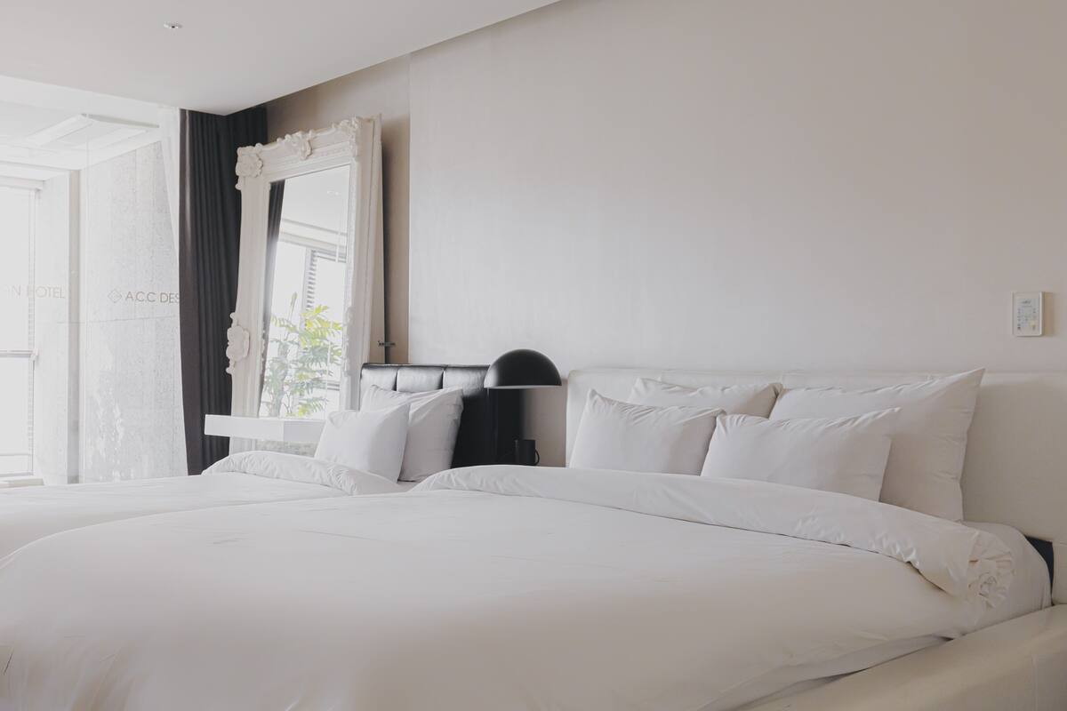 Una habitación de hotel moderna con una cama grande, una mesita de noche, un espejo y una ventana con cortinas.
