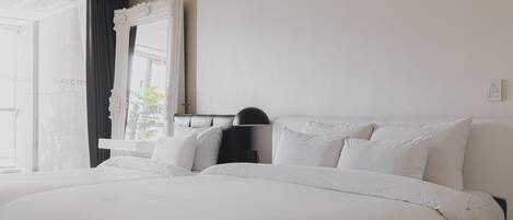 Una habitación de hotel moderna con una cama grande, una mesita de noche, un espejo y una ventana con cortinas.