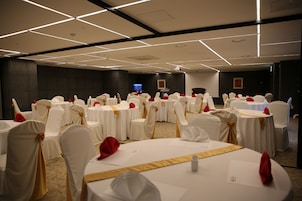 Un salón de banquetes con mesas redondas y sillas, cada uno decorado con manteles blancos y fajas doradas.