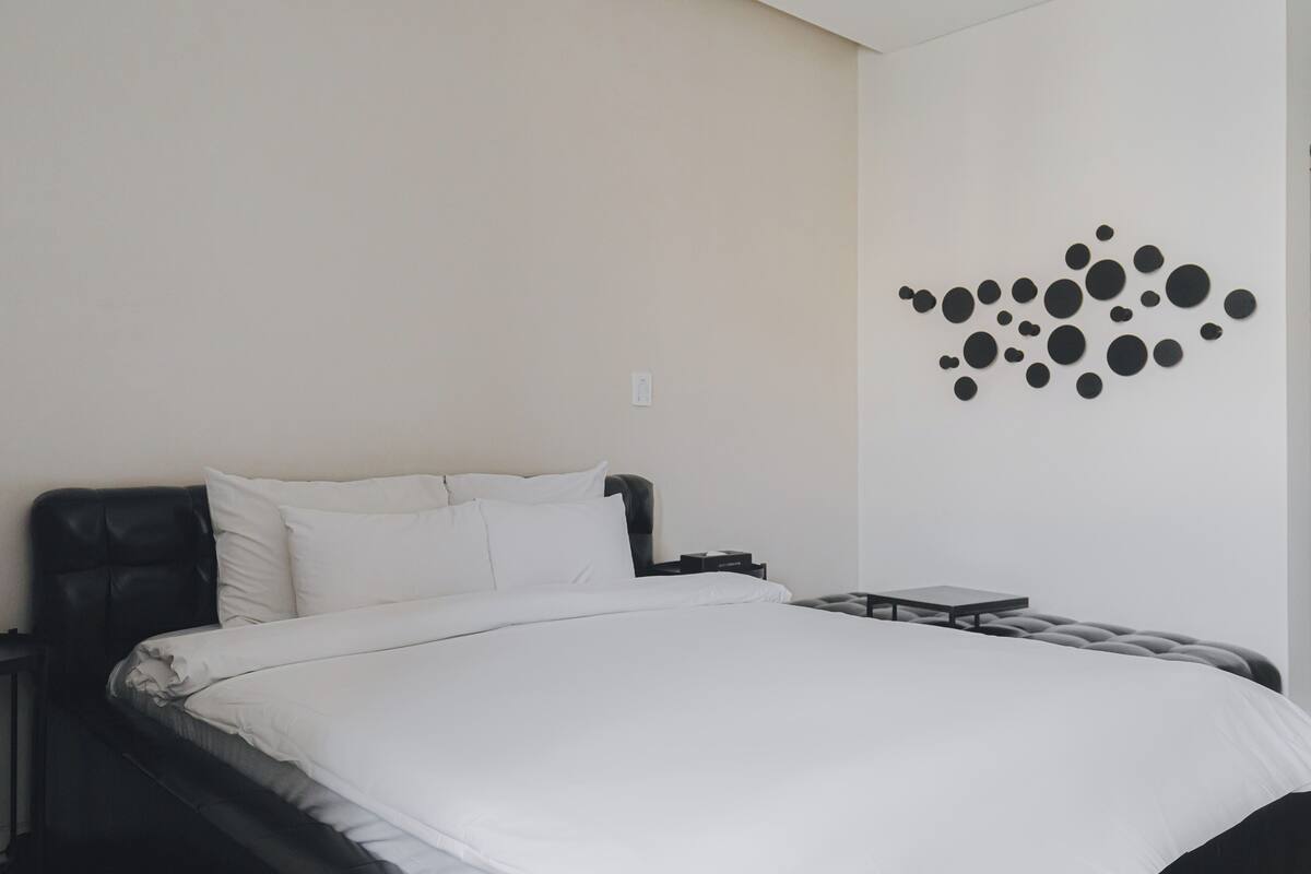Un dormitorio con cama, mesita de noche, lámpara de pared y una pequeña mesa.