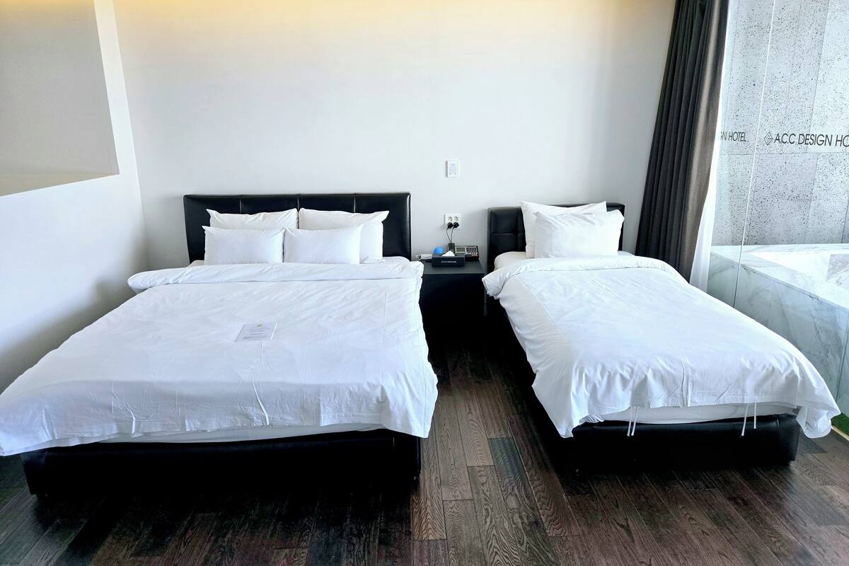 Habitación de hotel con dos camas, una mesita de noche, una lámpara y un ventanal con cortinas.
