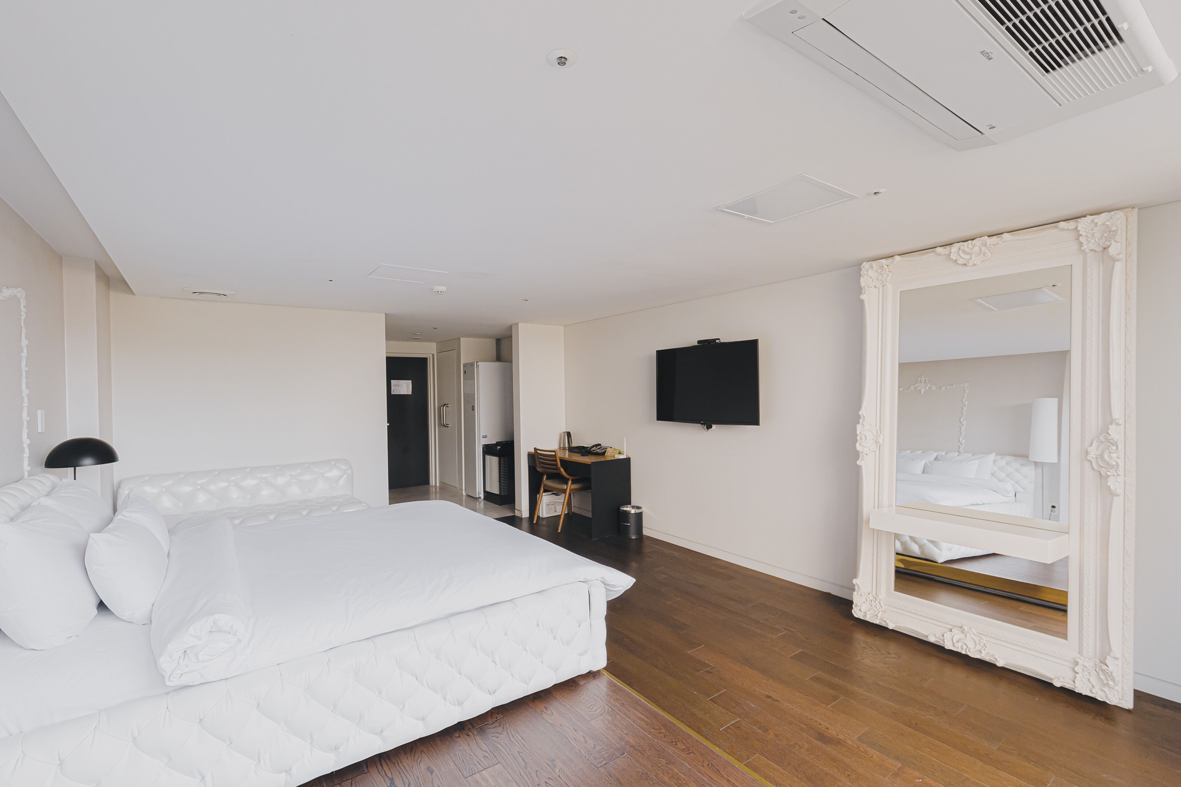 Quarto moderno com cama grande, escrivaninha e TV fixada na parede.