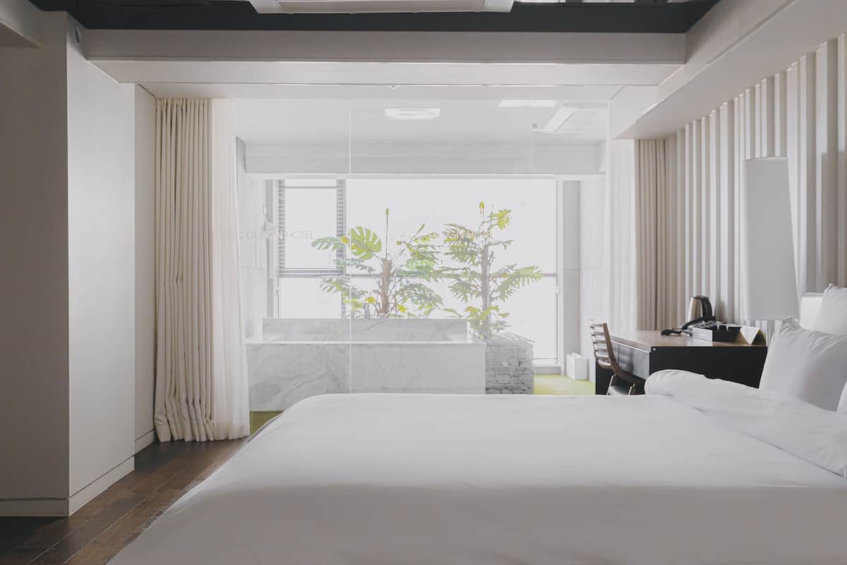Una habitación de hotel moderna con una cama grande, un escritorio con lámpara y vistas a zonas verdes por la ventana.