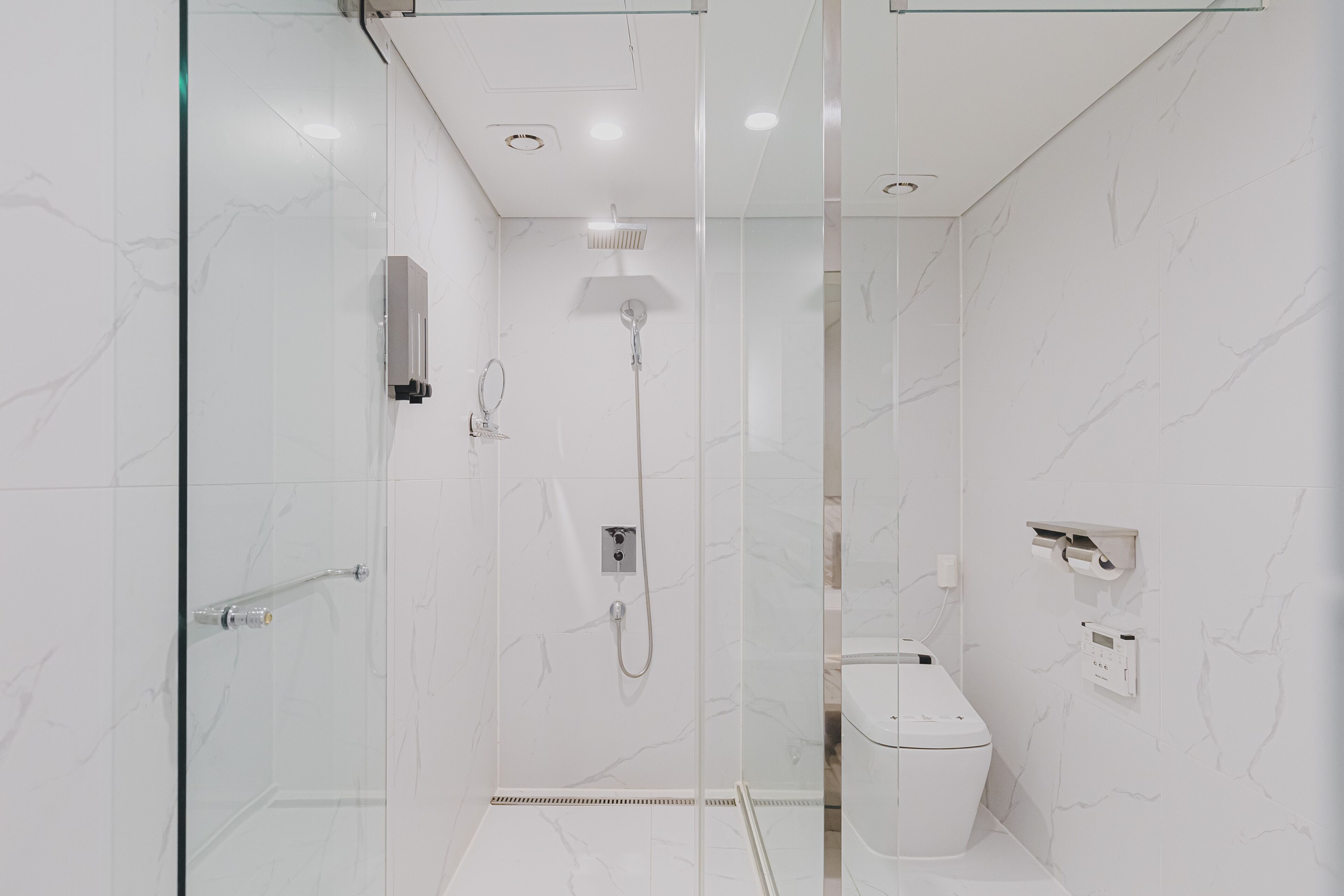 Ein modernes Badezimmer mit Duschkabine aus Glas, Toilette und Bedienfeld an der Wand.