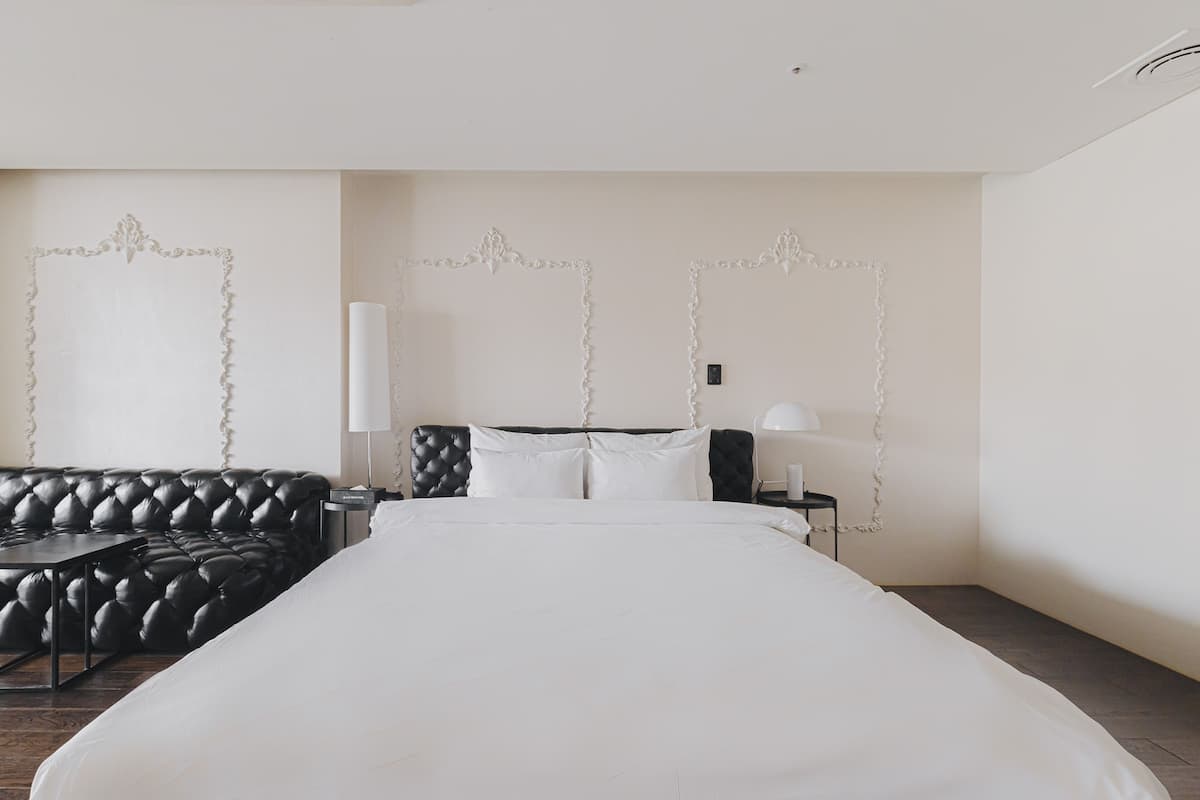 Una habitación de hotel con una cama grande, un sofá de cuero negro, una mesita de noche con lámpara y paneles decorativos en la pared.