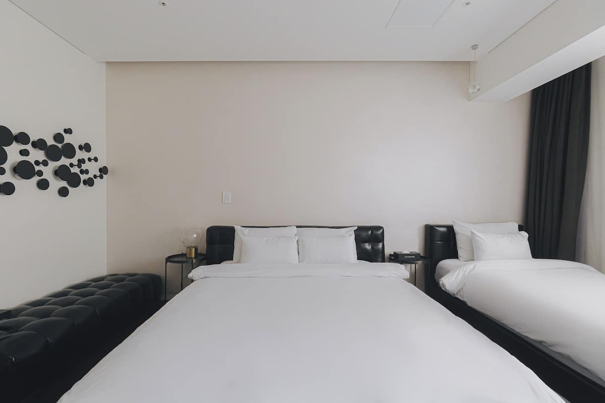 Habitación de hotel con una cama grande, un sofá negro, un aplique de pared y una ventana con cortinas.
