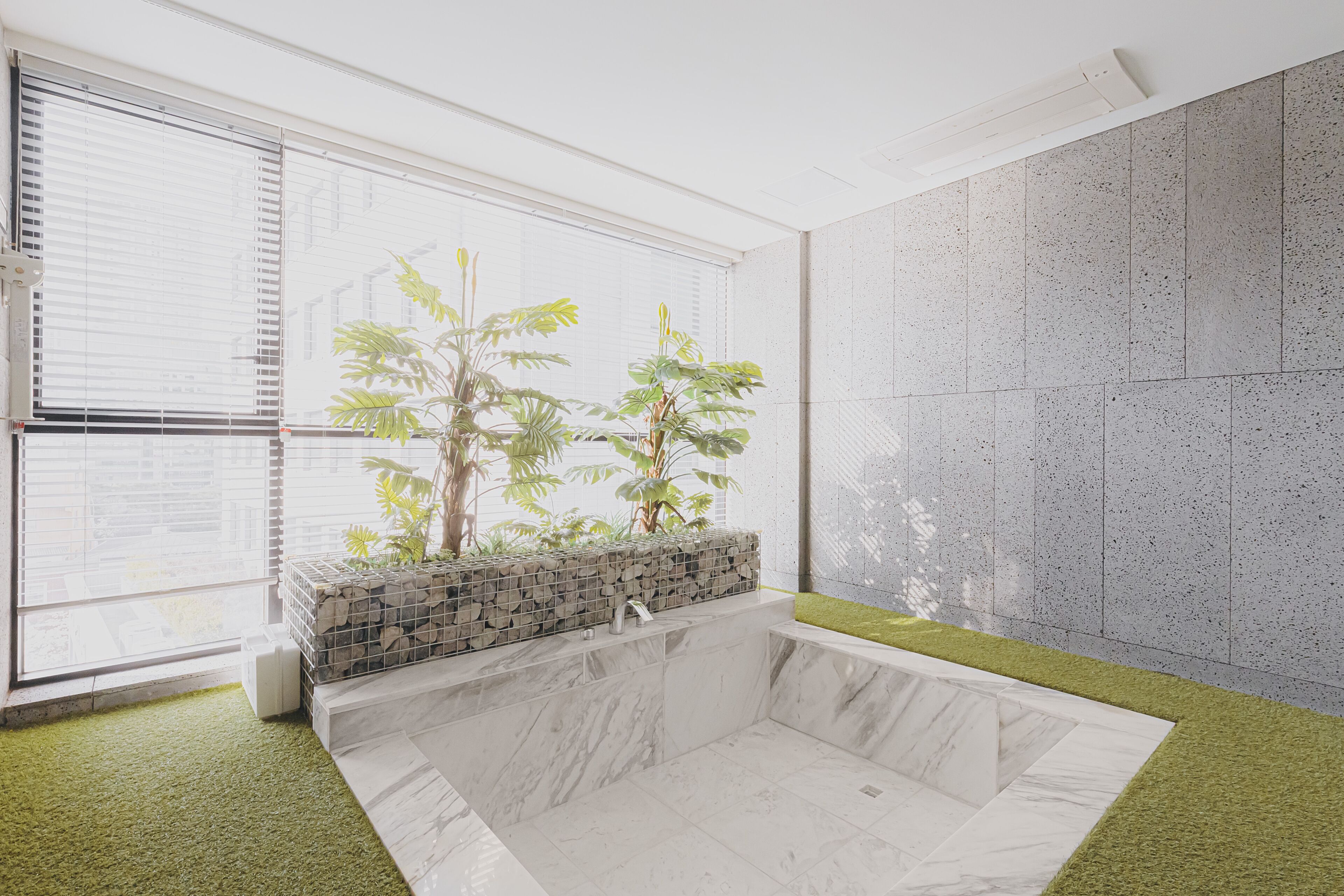 A modern bathroom with a marble tub, a small plant arrangement, and a view of the outside through large windows.