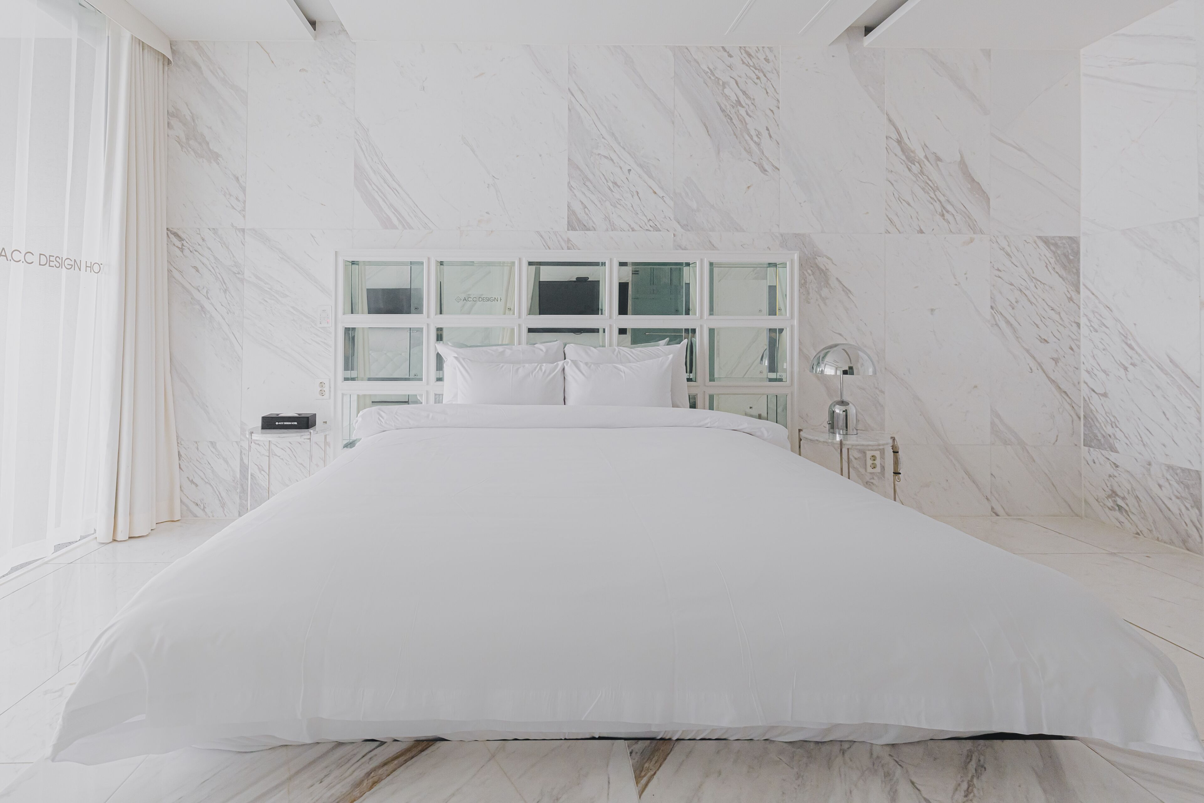 A modern bedroom with a large bed, marble walls, and a glass-fronted headboard.