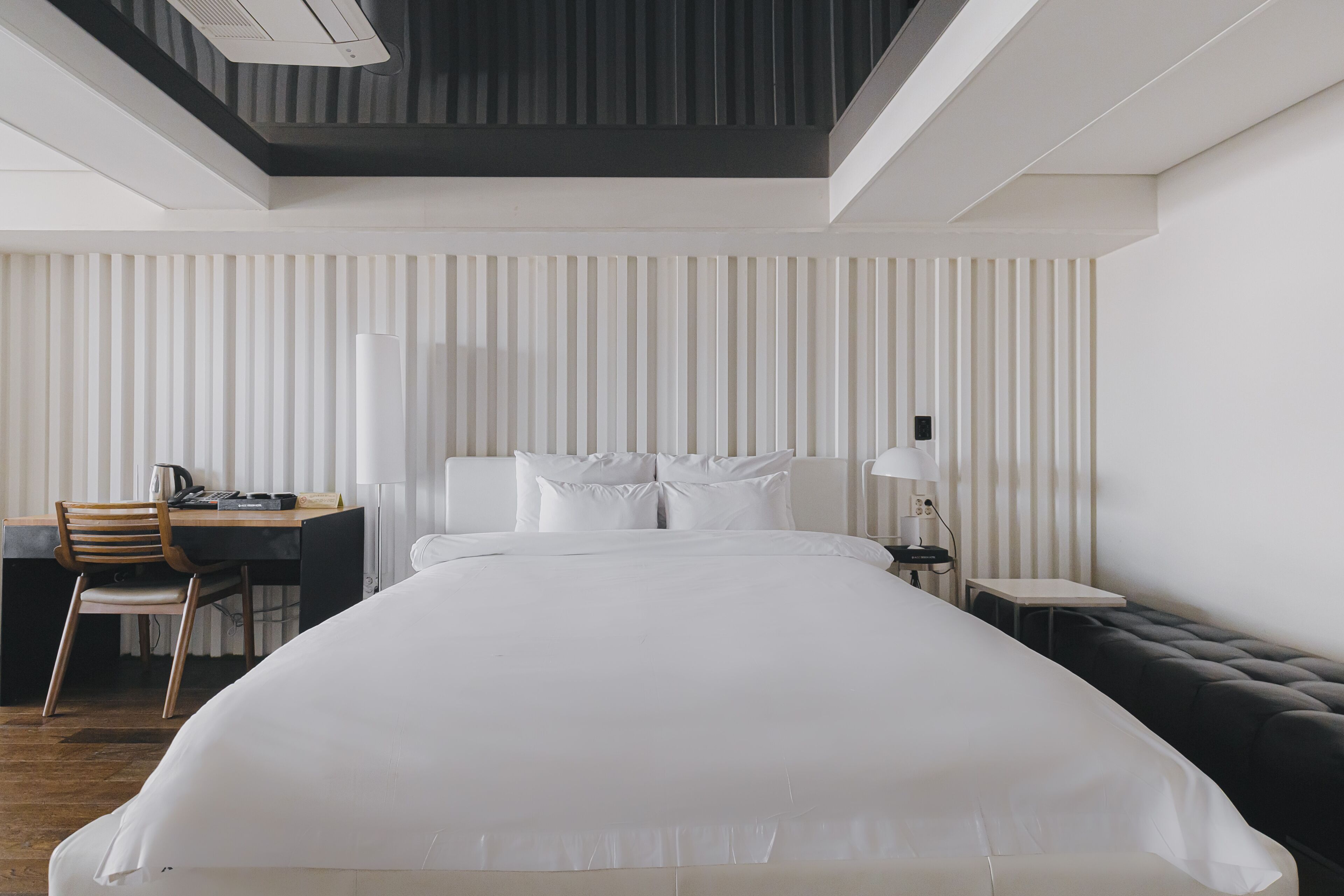 Una habitación de hotel moderna con una cama grande, un escritorio con silla, una mesita pequeña y un banco.