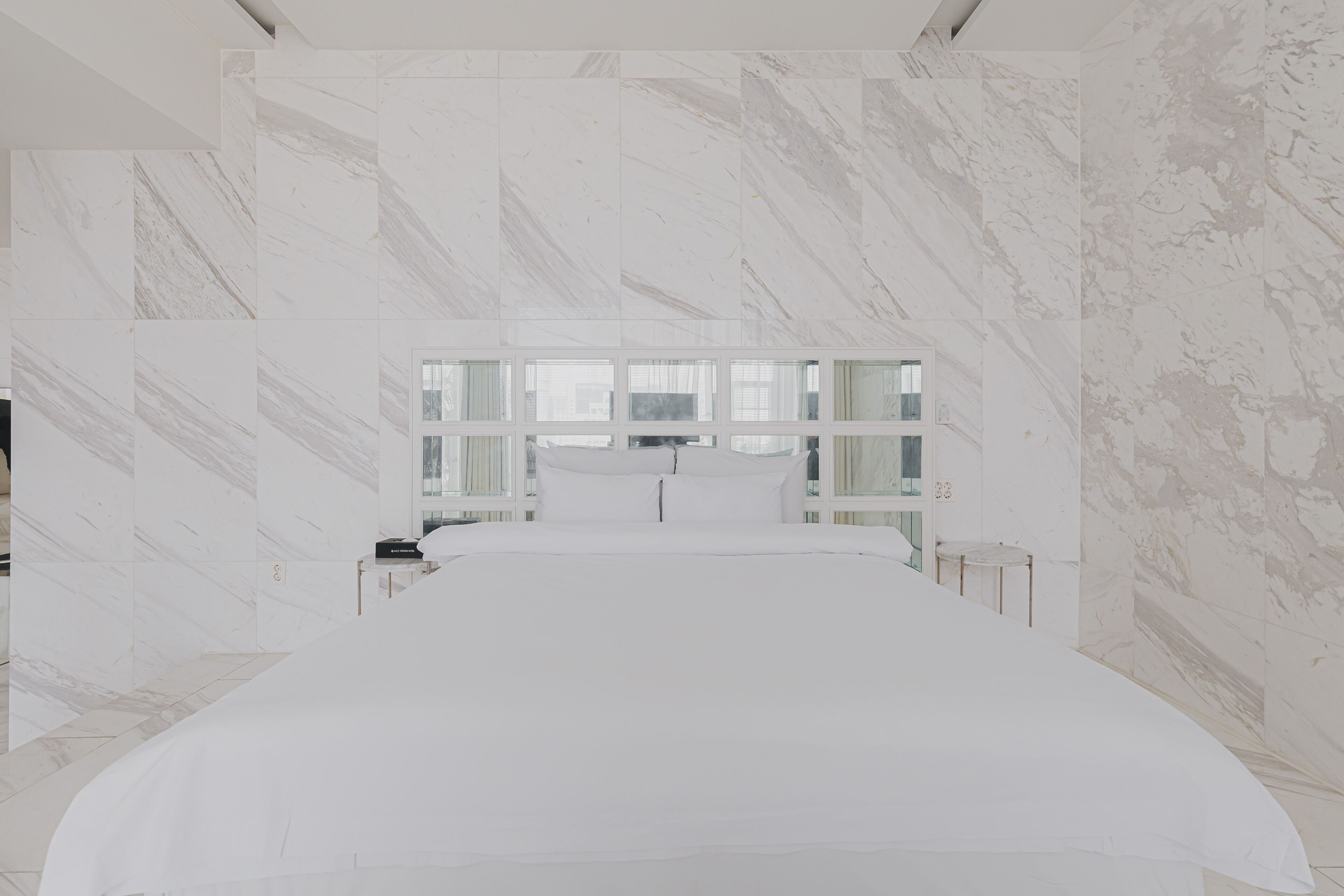 Une chambre d’hôtel moderne dotée d’un grand lit, de murs en marbre et d’une grande fenêtre offrant une vue sur la ville.
