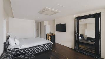 Ein modernes Hotelzimmer mit einem großen Bett, einem Schreibtisch, einem Sessel, einem Flachbildfernseher und einem großen, verzierten Spiegel.