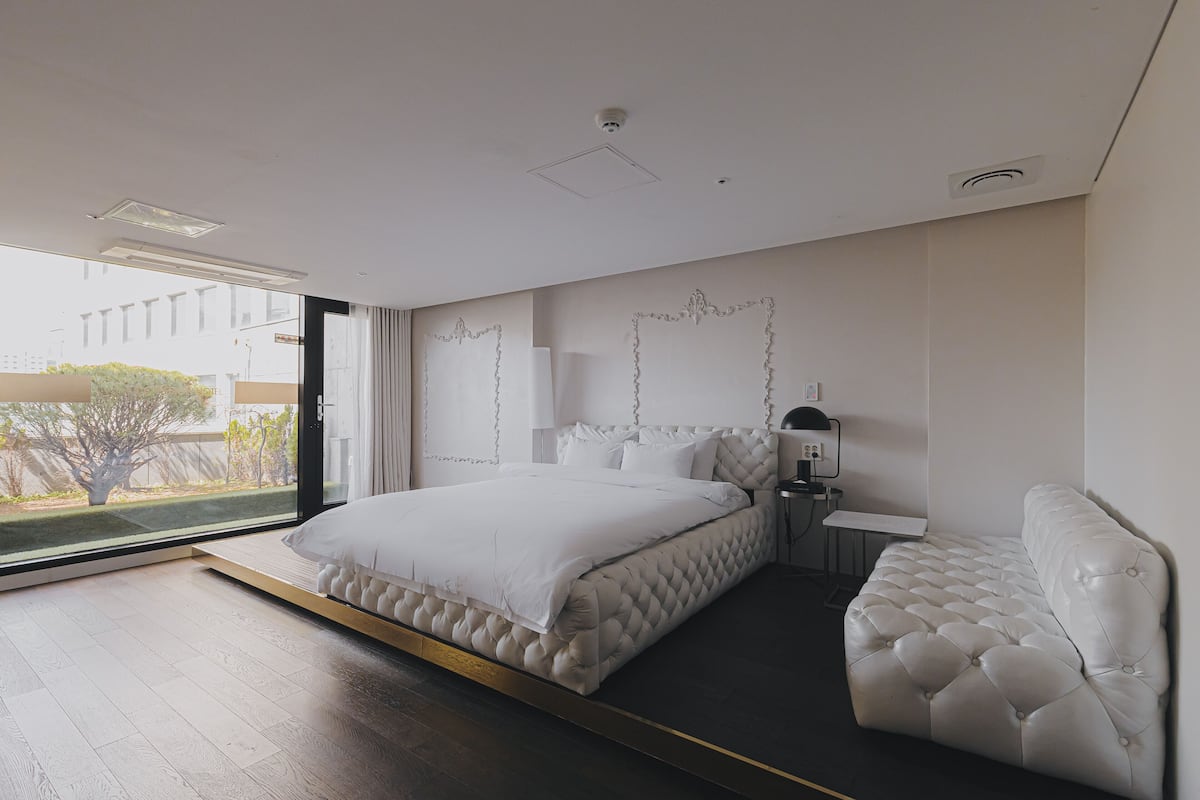 Un dormitorio moderno con una cama grande, una mesita de noche, una lámpara y vistas al exterior.