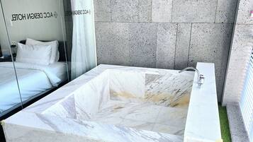 A modern hotel room with a large marble bathtub, a glass partition, and a green artificial turf floor.