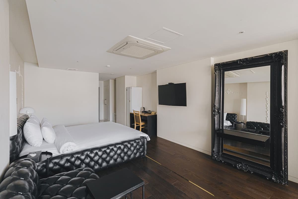 Habitación de hotel moderna con una cama grande, un escritorio, un televisor de pantalla plana, un espejo amplio y un suelo de madera oscura.
