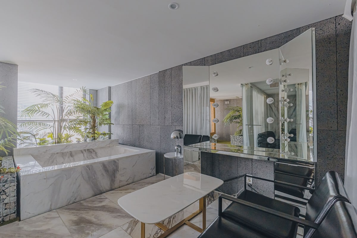 Un baño moderno con una bañera de mármol, un tocador de vidrio y un espejo grande.