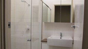 Een badkamer met een douchecabine van glas, een witte wastafel en een spiegel boven de wastafel.