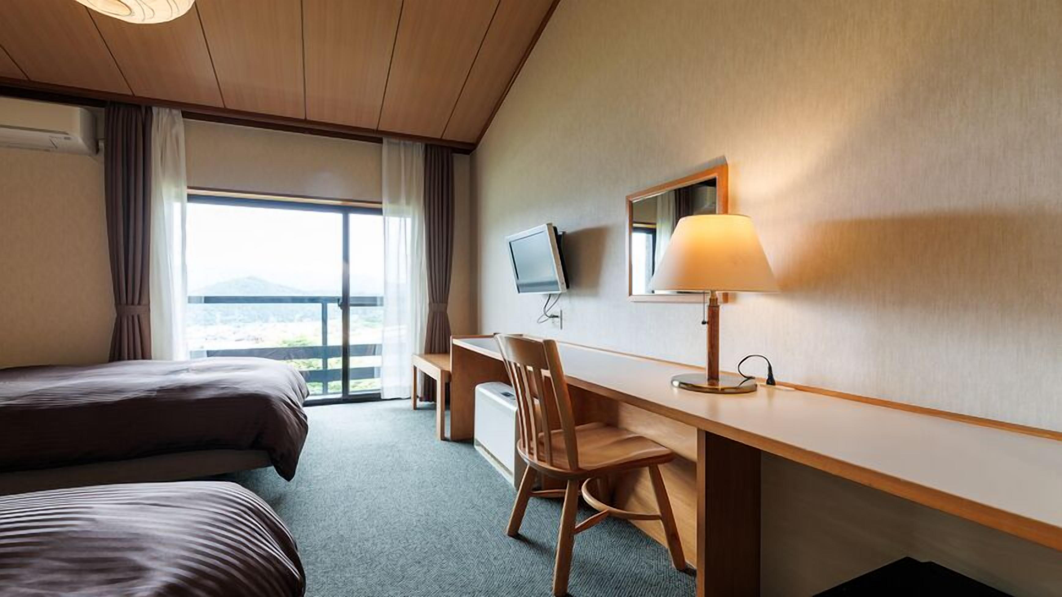 Habitación de hotel con cama, escritorio, silla, televisor y ventana con cortinas.