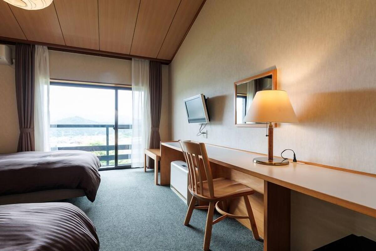 Une chambre d’hôtel avec un lit, un bureau, une chaise, une télévision et une fenêtre avec des rideaux.