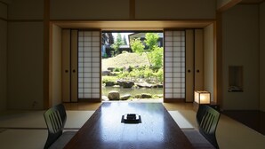 A traditional Japanese room with tatami flooring, a low table, and sliding doors leading to a garden view. - Hotel Kikori (Hida)