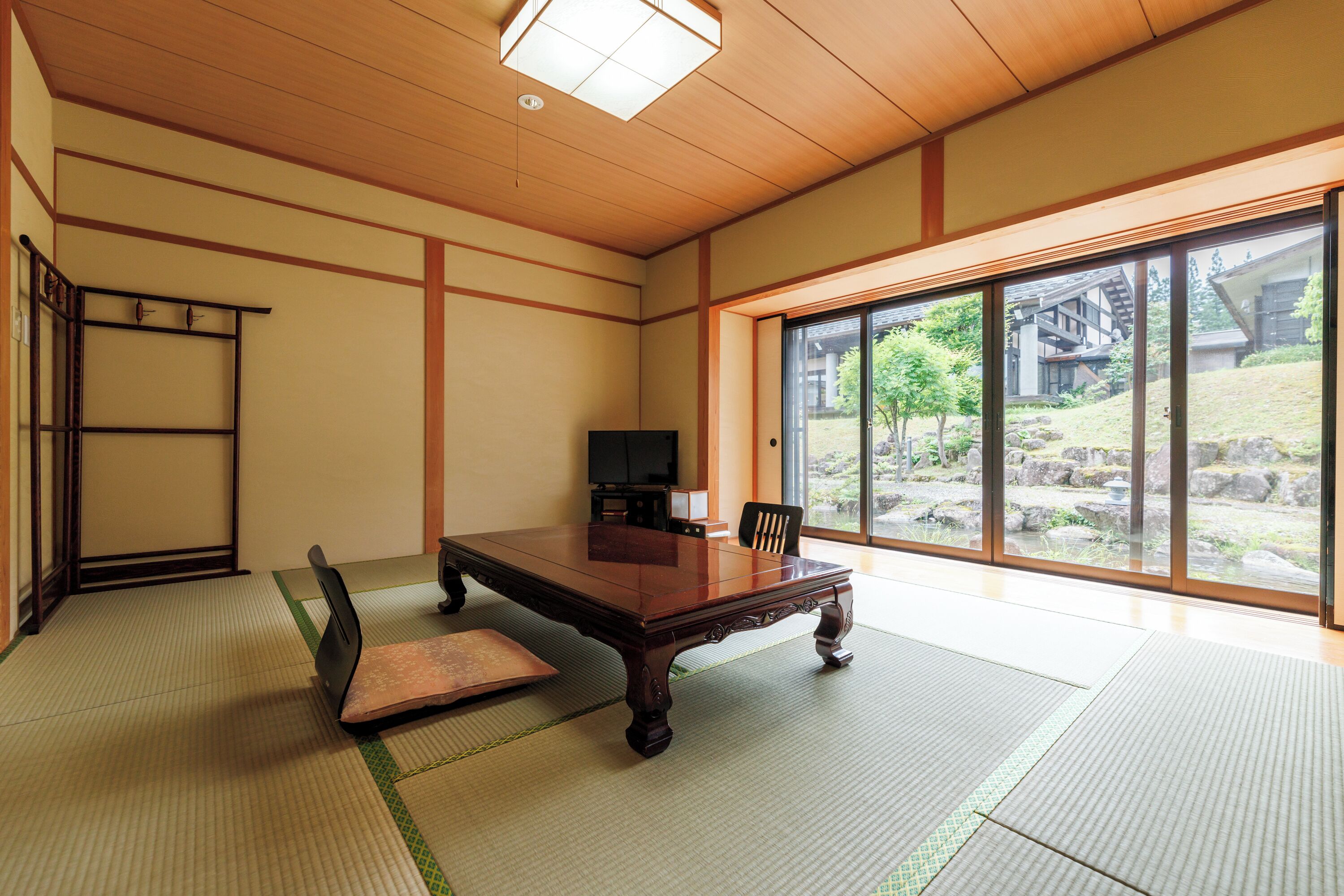 Een traditionele Japanse kamer met tatami vloerbedekking, een houten tafel en een schuifdeur naar een tuin.