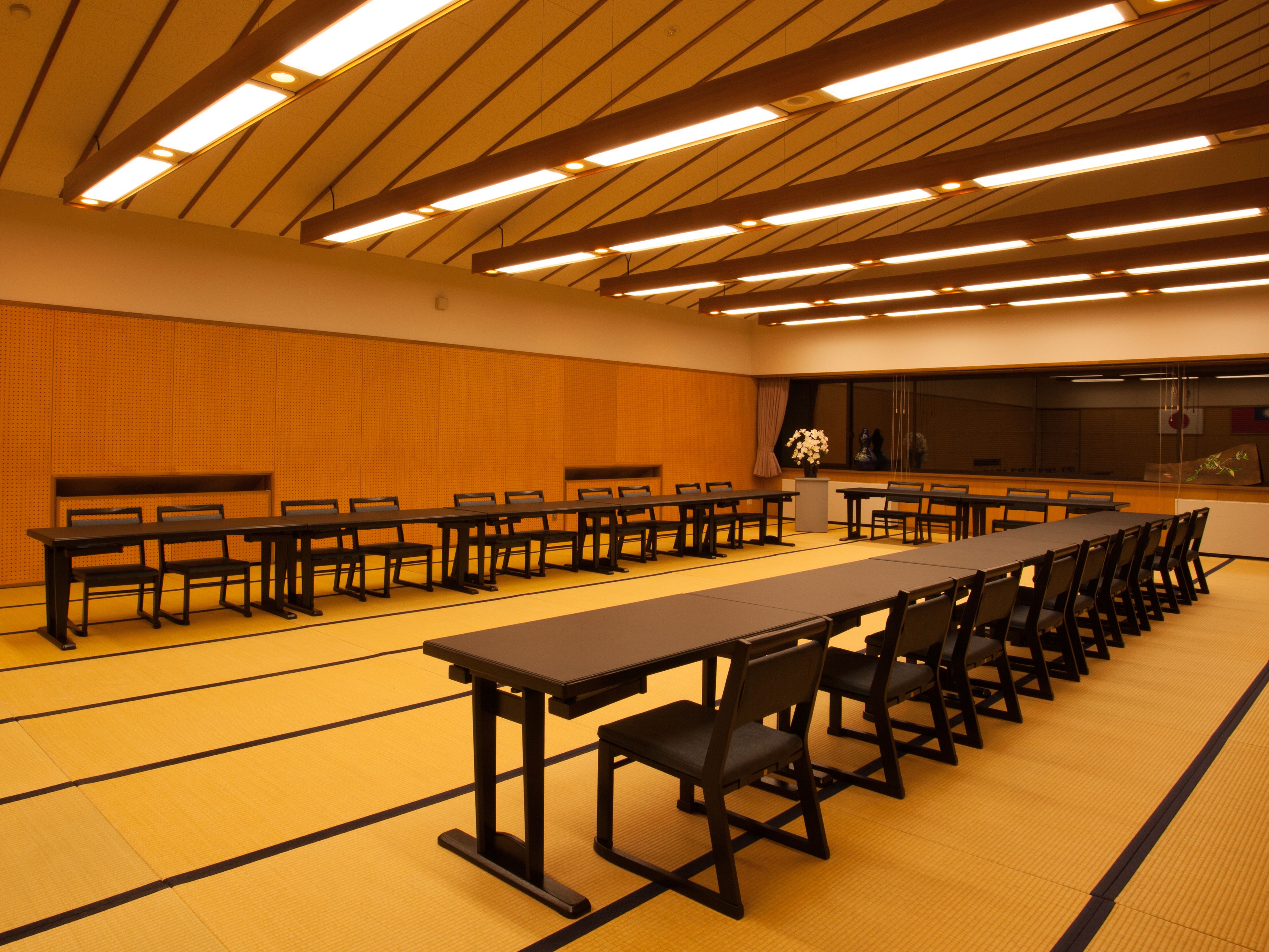 A conference room with long tables and chairs, a podium, and a large window.