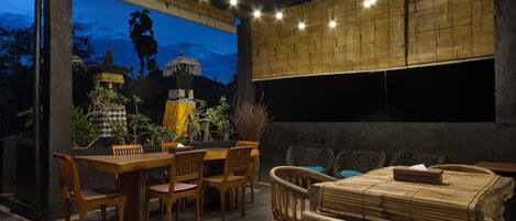 An outdoor dining area with a bamboo wall, wooden furniture, and string lights.