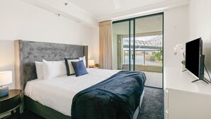 A hotel room with a large bed, a flat-screen TV, a desk, and a balcony with a view of a bridge.