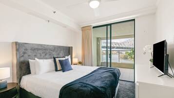A hotel room with a large bed, a flat-screen TV, a desk, and a balcony with a view of a bridge.