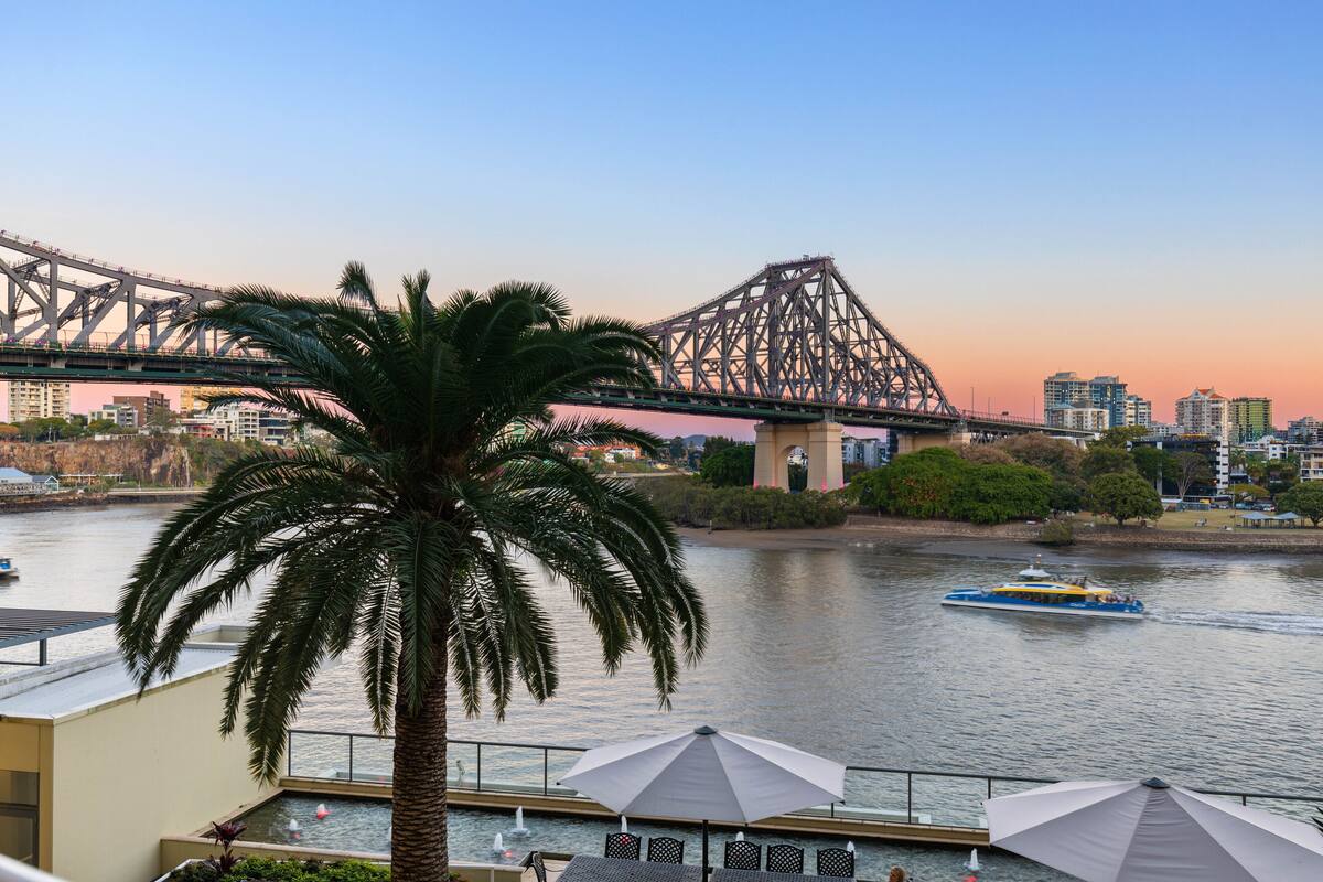 A waterfront view with a bridge, palm trees, and a boat on the water.