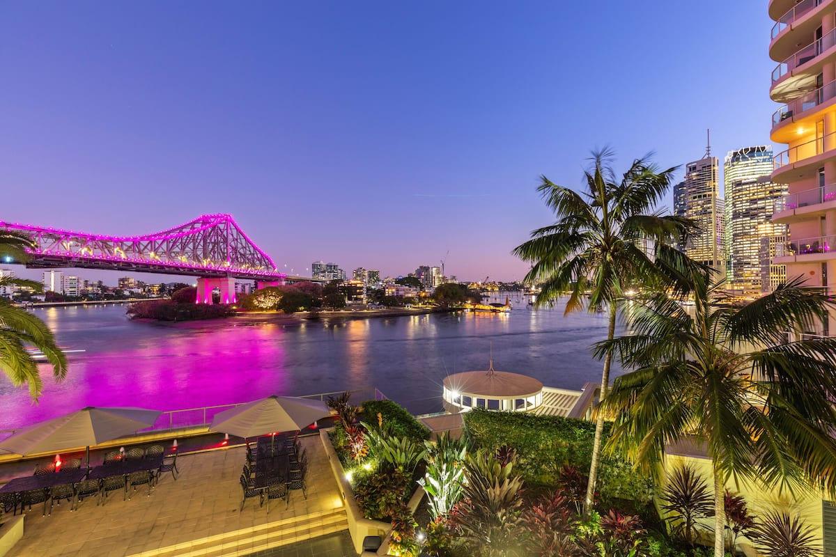 A waterfront hotel with a view of a bridge, palm trees, and a cityscape.