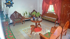 Une pièce comprenant un canapé en bois, une table ronde avec deux vases, une chaise en bois et un lit avec un rideau rouge.