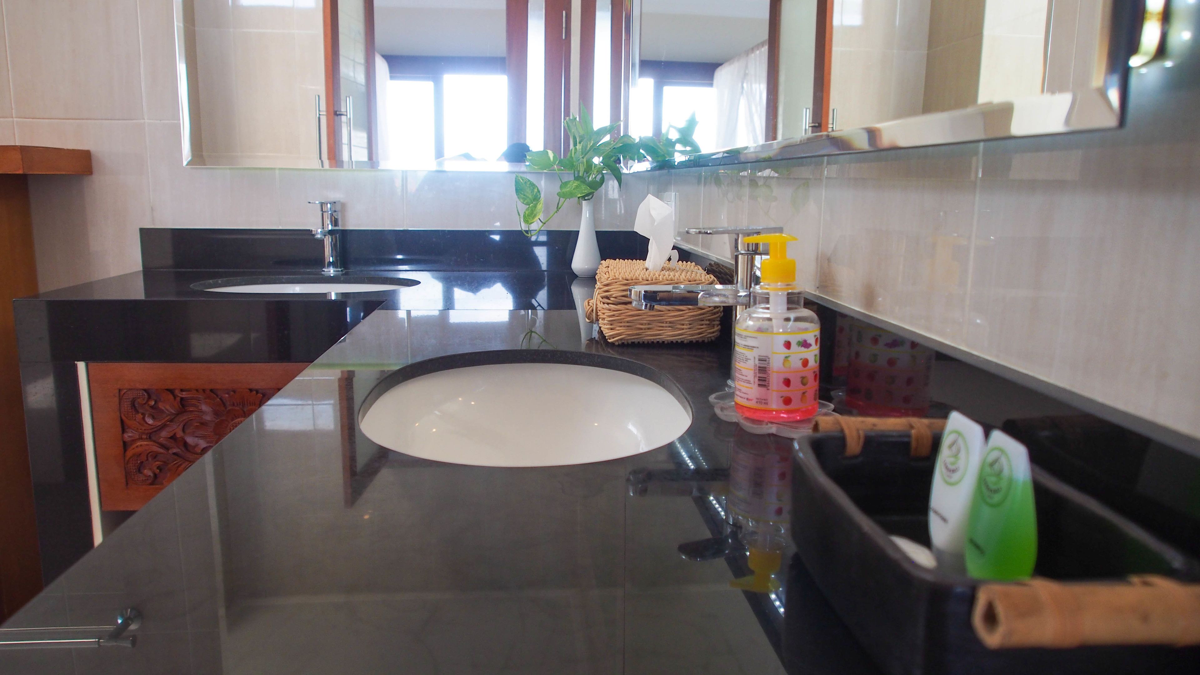 A modern bathroom with a black countertop, a white sink, and a large mirror. There is a wicker basket and a bottle of hand soap on the counter.