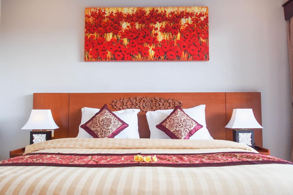 A hotel room with a large bed, two bedside lamps, a decorative headboard, and a floral painting on the wall.