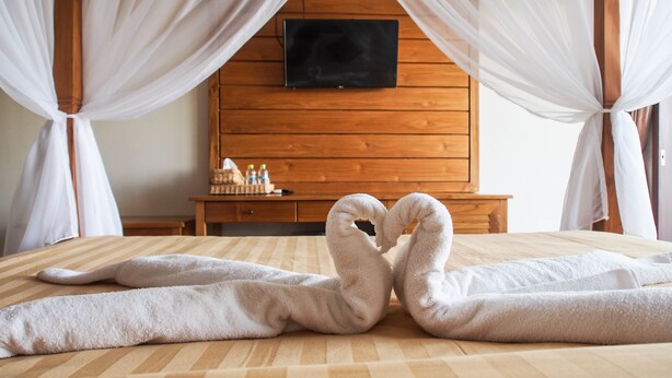 A hotel room with a bed, a wooden headboard, a TV mounted above it, and a bedside table with toiletries. - Lebak Bali Nelayan (Canggu)