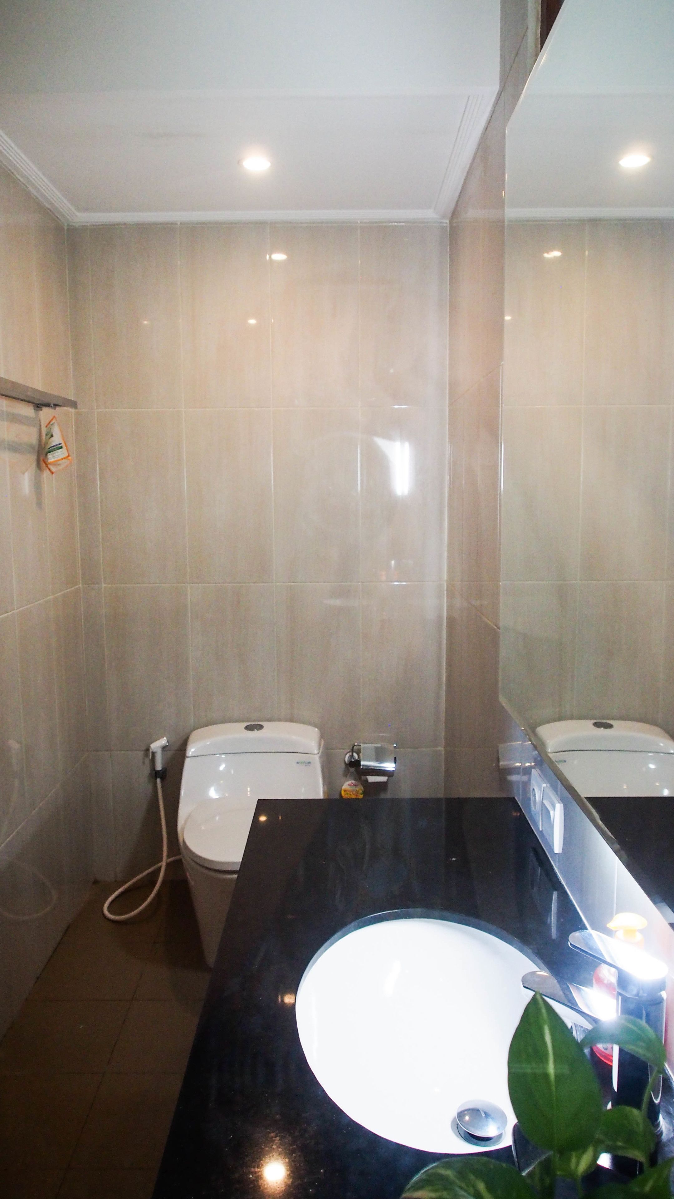 Une salle de bain avec un lavabo noir, des toilettes blanches et des murs recouverts de carreaux beiges.