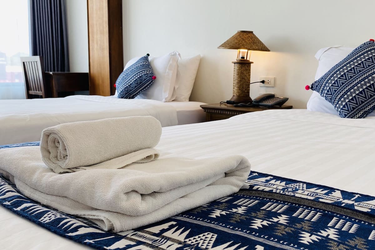 Ein Hotelzimmer mit zwei Betten, einer Lampe, einem Telefon und einem ordentlich gefalteten Handtuch auf dem Bett.