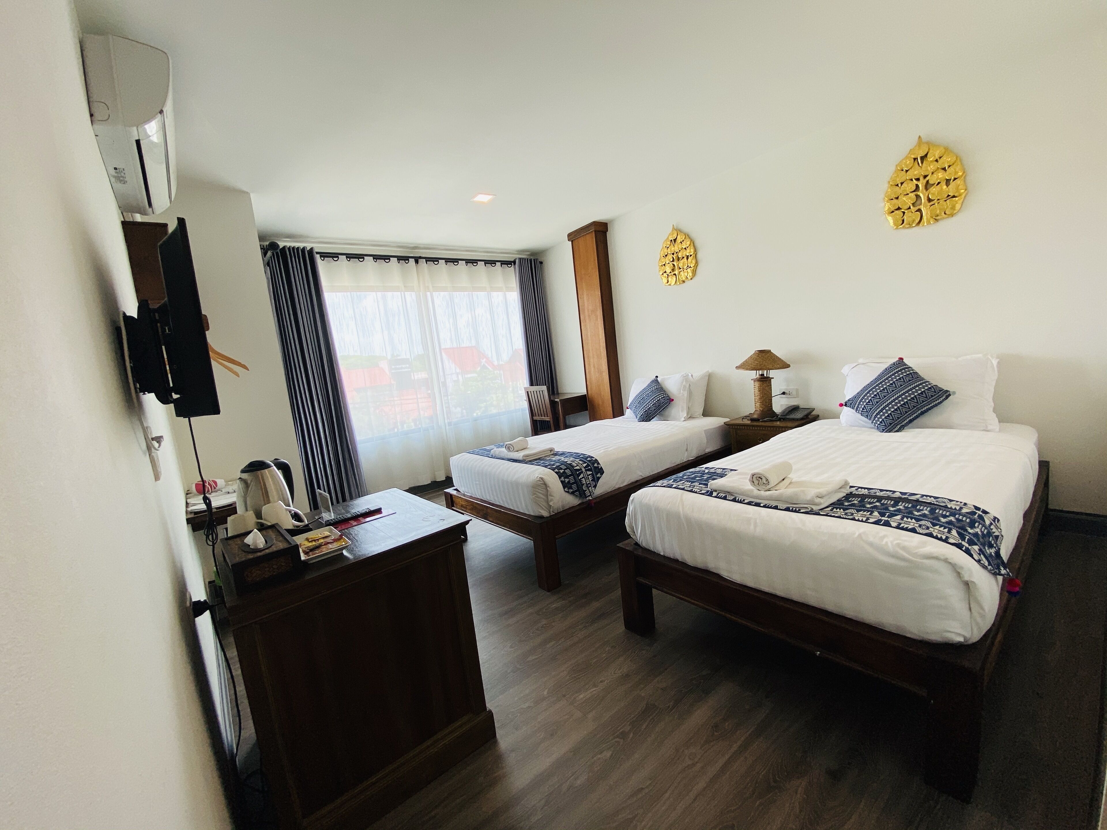 Habitación de hotel con dos camas, un escritorio con lámpara, televisión y ventana con cortinas.