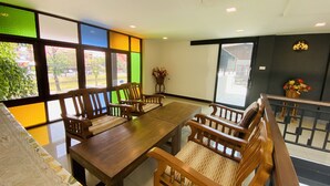 Un espace repas avec une table et des chaises en bois, de grandes fenêtres ornées de panneaux colorés et une vue sur l’extérieur.
